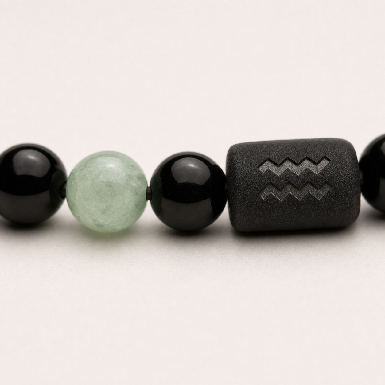 Close-up of the Aquarius zodiac symbol with obsidian and Tiger’s Eye beads